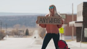 Woman holding anywhere sign hitchhiking on remote rural road / Loa, Utah, United States
