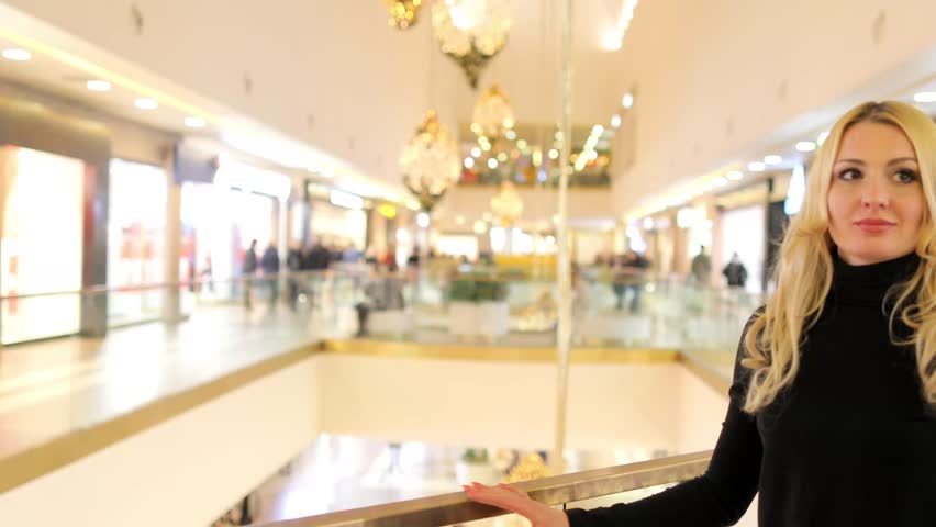 A beautiful blonde girl is walking in a large building, shoppers are walking.