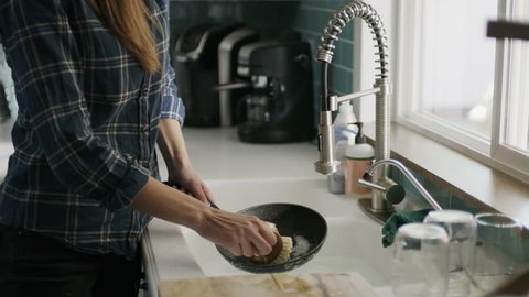 Woman washing pan talking on cell phone and dropping it into sink / Alpine, Utah, United States