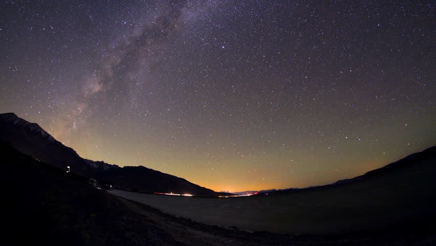 Milkyway cloud timelapse over water reflection, highway flashlights and mountains in the distance