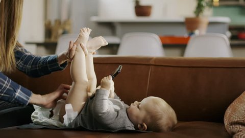 Mother changing diaper of baby daughter distracted with cell phone / Alpine, Utah, United States