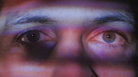 Close up eyes of a young man watching a video or film on TV or a computer monitor. Reflection on her face