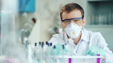 Handsome researcher in white coat is looking at camera while sitting in laboratory