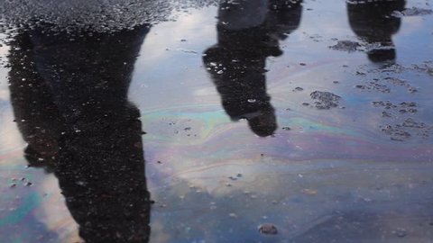 Slow-mo footage. Passing people are reflected in an oil puddle