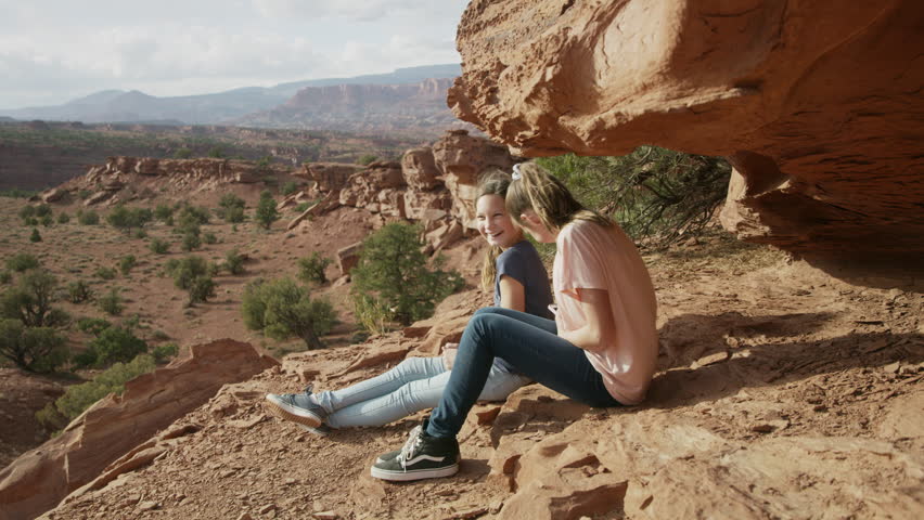 Girls sitting near rock formation and scenic view of desert landscape / Capitol Reef National Park, Utah, United States
