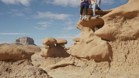 Girl sitting on the edge of rock formation in desert posing for cell phone selfie / Goblin Valley, Utah, United States