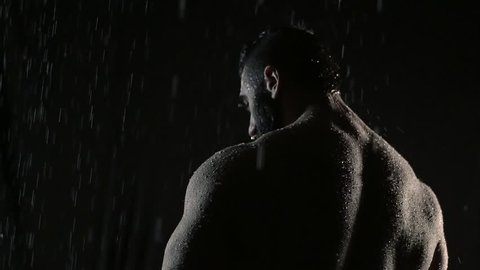 Powerful muscular man warrior stands in the rain with his back to the camera. he turns his head