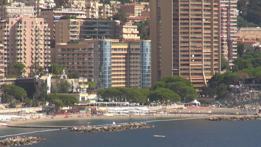 Aerial view of luxurious Monaco residential building by day, people relax on beach