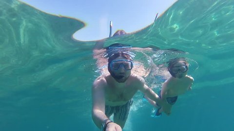 Father and son with flippers, mask, snorkel and a selfie stick swimming in the sea, gopro underwater footage