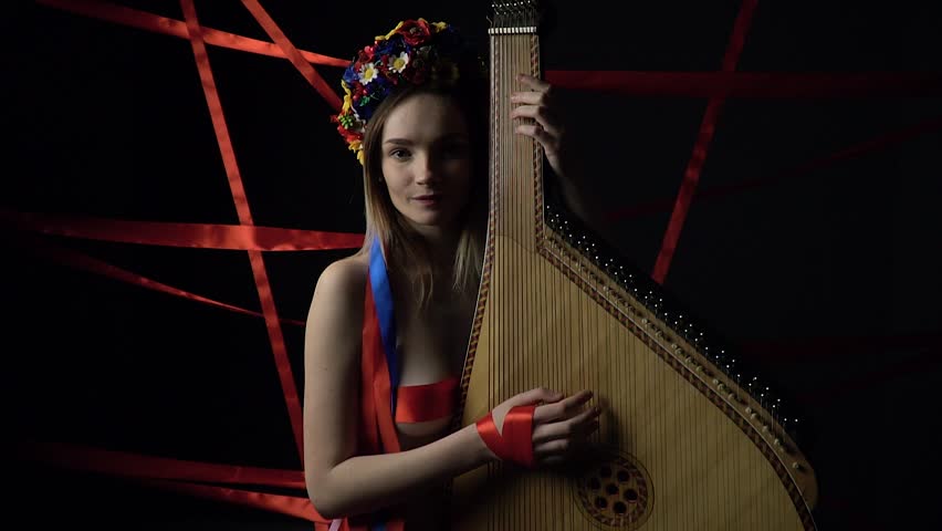 Girl playing on a bandura on a dark background with red ribbons