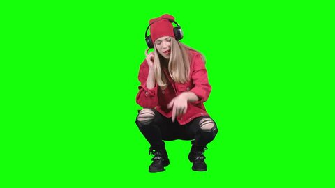 Girl sitting on her haunches and listening to music on headphones. Green screen