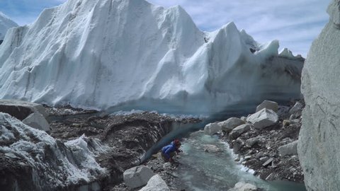 The Khumbu Glacier descends from Mount Everest. Walking on the glacier is very dangerous. A girl drinks water from a creek. Nepal. Himalayas. 4K