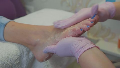 Professional beautician applying moisturizing cream before foot massage at the beauty spa salon, close-up in slow motion