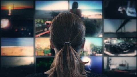 Watching TV Multi Screen Television. Head shot of a ponytail woman watching many videos in a wall of televisions