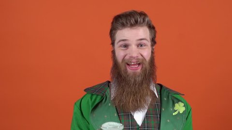 Young man leprechaun celebrating saint patrick's day isolated on orange wall offering green beer