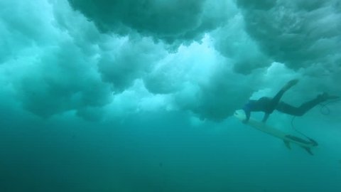UNDERWATER, SLOW MOTION: Brave male surfer paddling in deep water as wild waves crash above him. Extreme sportsman doing a duck dive in ocean. Awesome underwater shot of intimidating waves breaking.