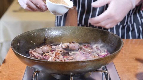 Close-up of Chef Cooking Flambe Style Dish with Slices of liver on a hot frying pan in restaurant. hand in glove adds cane sugar to the dish in frying pan. Slow motion.