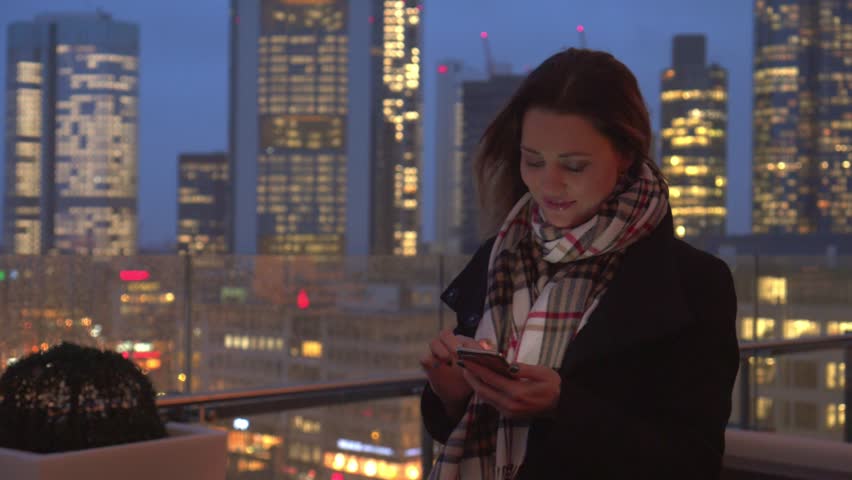 Beautiful woman in the city of Frankfurt at night with a smartphone and writes messages