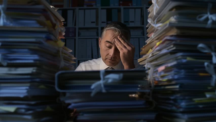 Tired businessman working late at night, he is overwhelmed by work and his desk is filled with paperwork, work overtime and deadlines concept Royalty-Free Stock Footage #1007116468