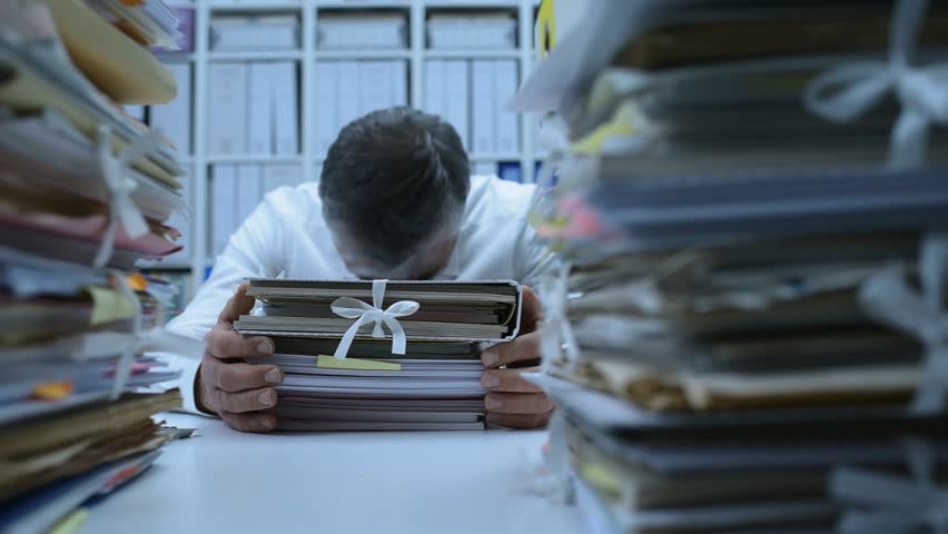 Frustrated overworked office worker hitting his head on a pile of paperwork: stress and work overload concept | Shutterstock HD Video #1007116519