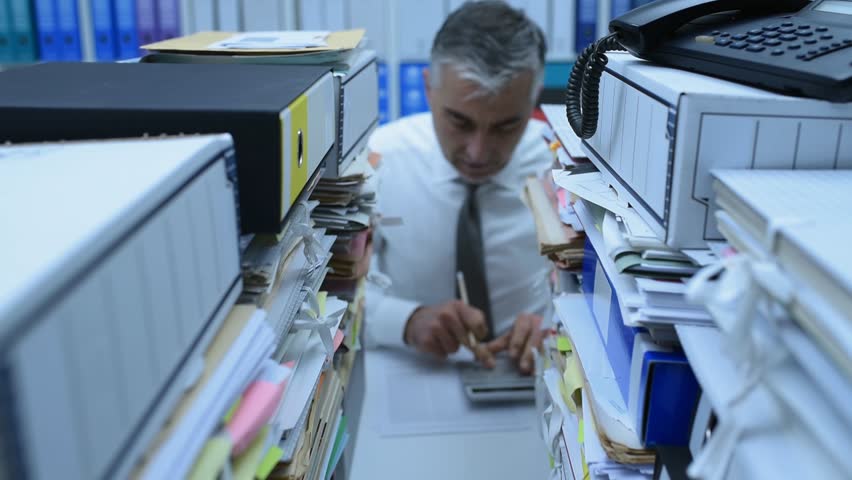 Overworked businessman working in the office and doing calculations, his desk is covered with paperwork, he is angry and screaming | Shutterstock HD Video #1007116540