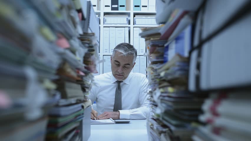 Business executive overwhelmed by work, he has piles of paperwork and files on his desk | Shutterstock HD Video #1007116558
