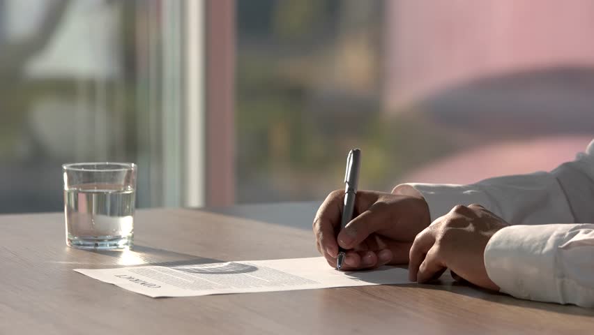 Deal concept, man signing contract and moving away. Peper signing in sunny office. Peper and glass of water on the table.
