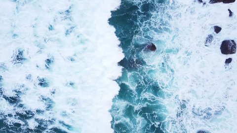 Top view moving up away ocean blue waves crash coastline cliff drone footage