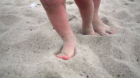 Little baby learns to walk. Close up on feet. Mother is teaching her child to do the first steps on beach sand in summer. Toddler is learning to walk, Slow Motion