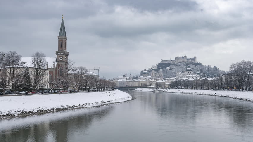 Day to night time-lapse footage of the historic city of Salzburg with famous beautiful Hohensalzburg Fortress reflecting in Salzach river with moving clouds in winter, Salzburger Land, Austria