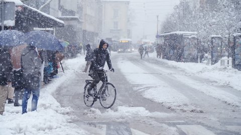 LJUBLJANA, SLOVENIA - JANUARY 2018: Person bicycling in city snow blizzard slow motion 4K. Wide view of Ljubljana city center road with a single bicyclist in focus driving over the dangerous road.