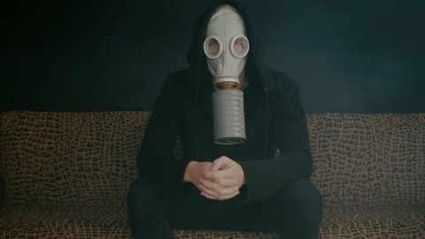 Man in a gas mask sitting in smoke in a dark room. Stalker in the post-apocalyptic world