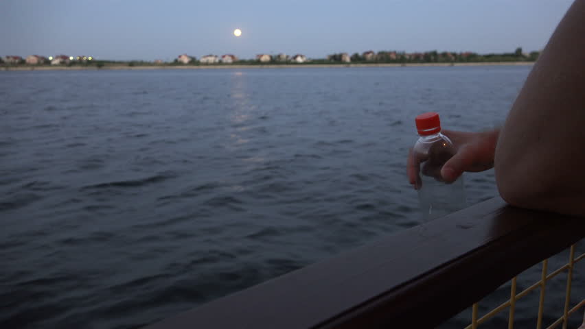 a sailor holding a plastic bottle with a red lid standing on the deck.