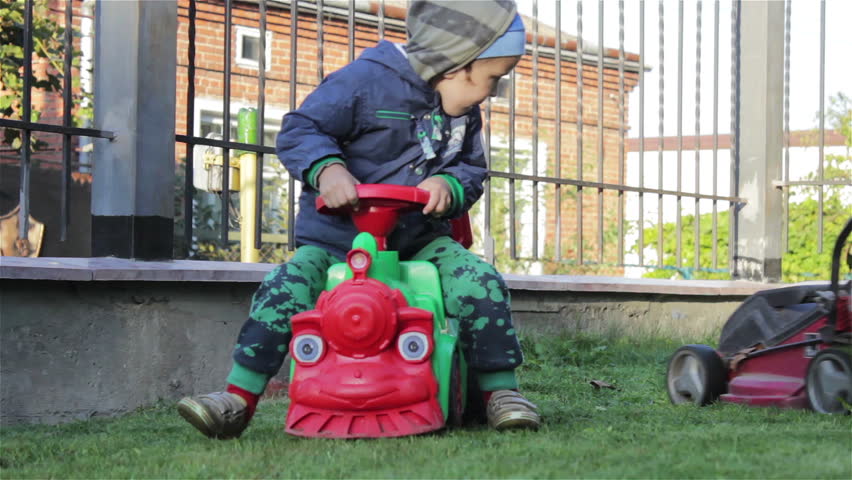 little boy sitting on toy car,in the yard on the grass the boy sitting on toy car
