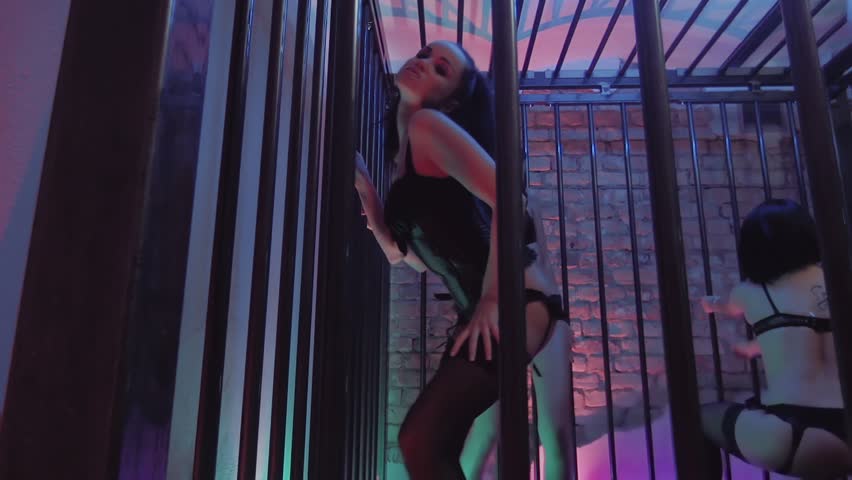 Sexy young caucasian brunette girls group alluring dances in black maiden lingerie in night club cage with metal bars. Colorful purple and green lights on brick wall | Shutterstock HD Video #1007176576