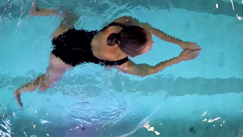 Young woman swims breaststroke in the pool in slow motion. The camera is just above her head. She's very pretty and slim. Swiiming is the way to stay fit/Young Woman Swimming Breaststroke in the Pool  | Shutterstock HD Video #1007181181