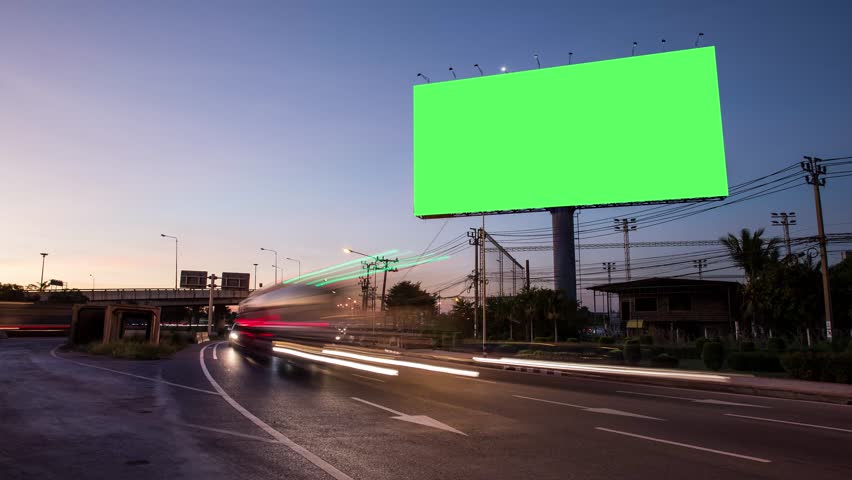 Advertising billboard green screen on sidelines of expressway with traffic at evening, time lapse.