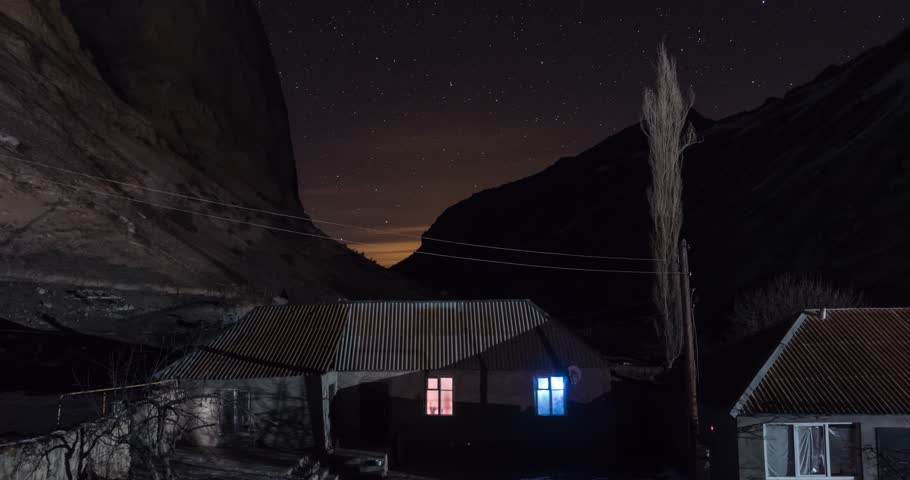 Stars over the house in the village in the mountains. Light in the window of a house in the night