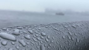 Raindrops clinging to a round metal railing with a foggy river view in the background