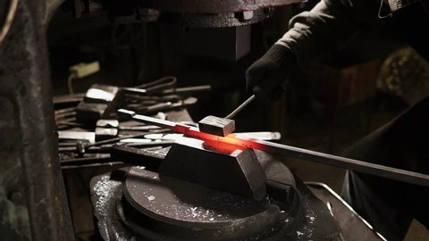 Process of forming red hot metal rod in a forge with automatic molder. Blacksmith is using metal instrument for smooth forms.