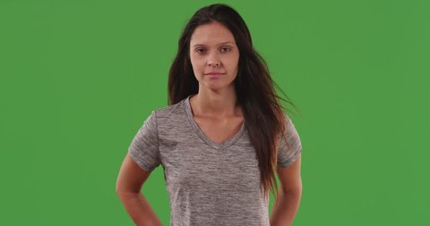 Healthy attractive young woman posed with long black hair blowing on green screen. Lovely caucasian woman standing with arms on waist in front of greenscreen wall. 4k