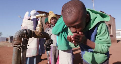 Poverty.Inequality.Poor people in Africa unable to maintain social distance. Young African boys drinking water from a communual tap while woman line up to collect water in plastic containers 