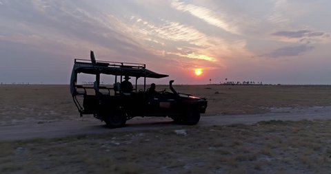 Aerial view of a 4x4 safari vehicle driving through the Makgadikgadi Pans with the sun setting in the background, Botswana