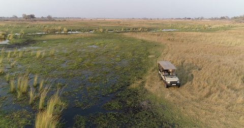 Aerial close-up zoom out view of a tourist 4x4 vehicle driving nex to one of the many waterways of the Okavango Delta, Botswana Stockvideo