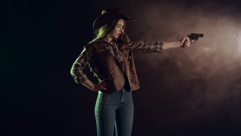 Sheriff girl holds a revolver in her hands and aiming at the villain. Black smoke background. Slow motion. Side view