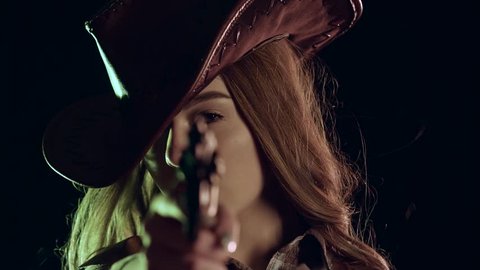 Sheriff girl holds a revolver in her hands and aiming at the villain. Black background. Slow motion. Close up