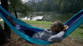 Caucasian female relaxing on hammock by the lake, shot in a mountain region in Switzerland. People taking the time to breathe it all in, wellbeing. 