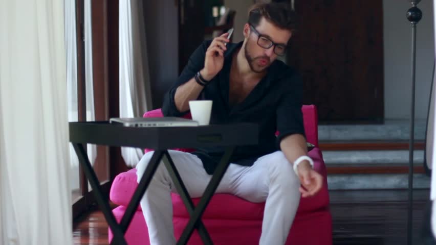 Handsome young man talking on the mobile phone and smiling while playing with dogs.