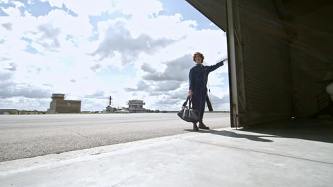 Zoom in of smiling female aircraft mechanic in uniform opening folding door and walking into hangar