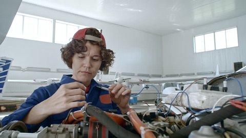 Professional female maintenance mechanic attaching testing device to airplane engine in hangar